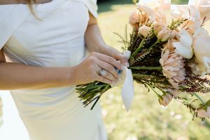 Elegant white wedding bouquet with cream roses and delicate greenery against a light outdoor background.