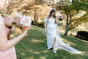 A bride in a flowing white dress poses elegantly in a sunlit autumn garden setting for wedding photos.