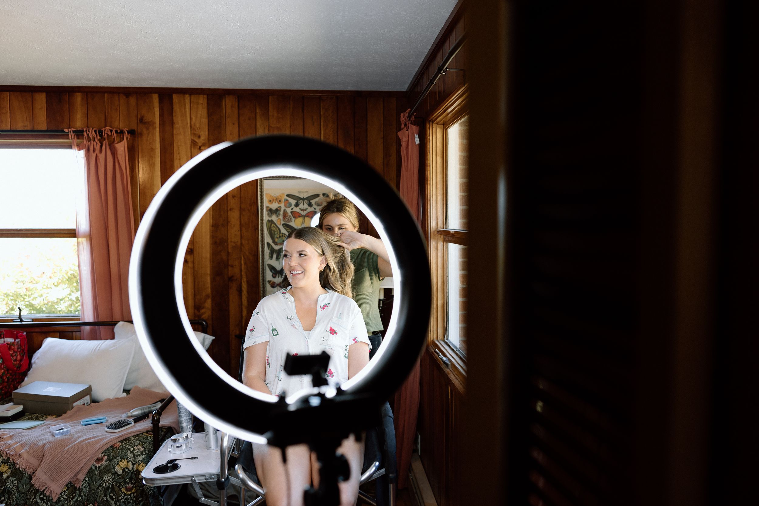 Person getting ready with a ring light and mirror for a special occasion in a wooden-paneled room.