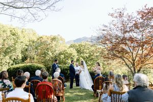Outdoor wedding ceremony with guests seated on vintage chairs surrounded by autumn trees and mountains.