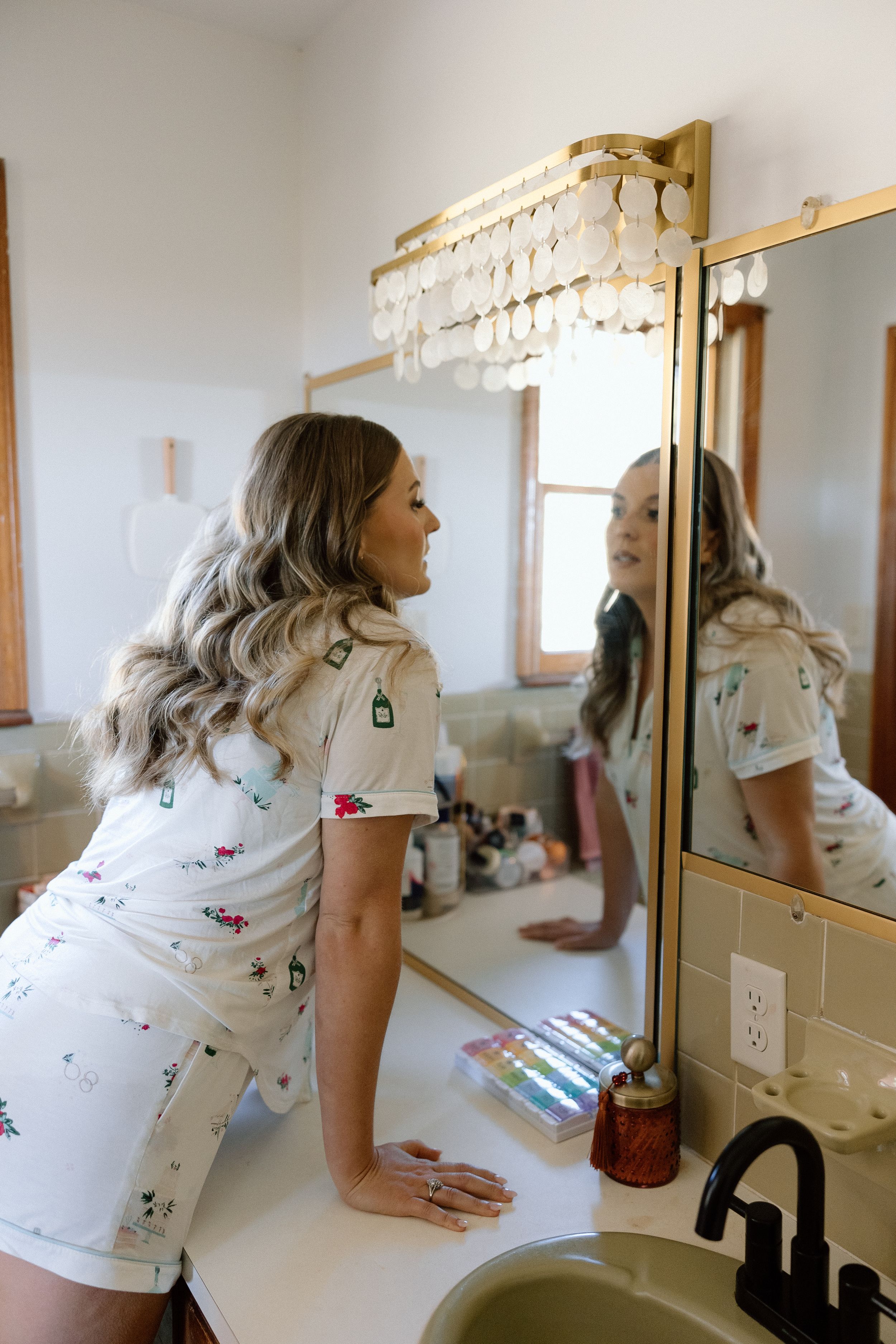 Person in a white floral dress leaning over a bathroom vanity with gold fixtures and mirror.
