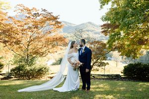 A couple shares an intimate moment in their wedding attire against a backdrop of golden autumn foliage and mountains.