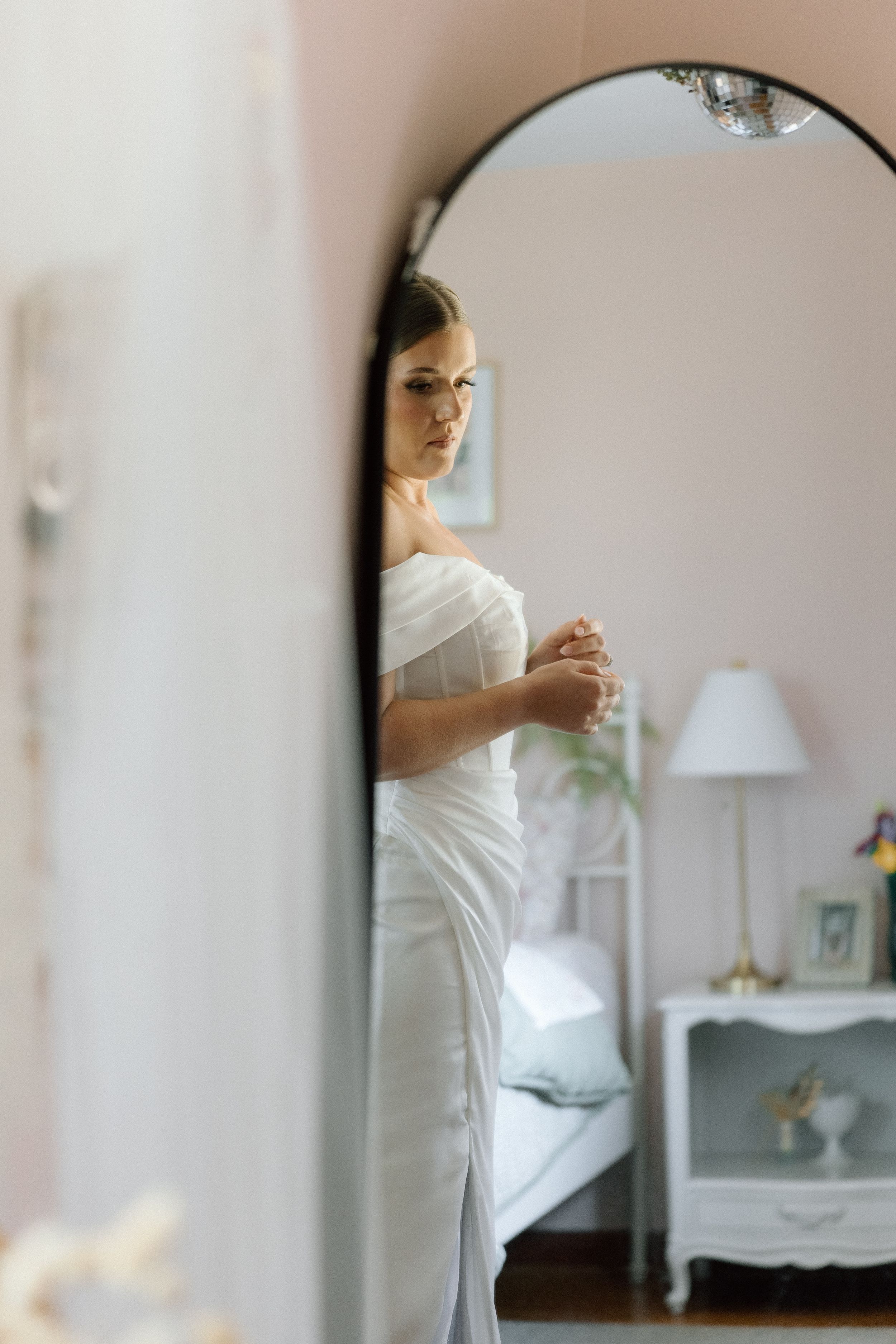 Reflection of bride in white dress getting ready in vintage mirror.
