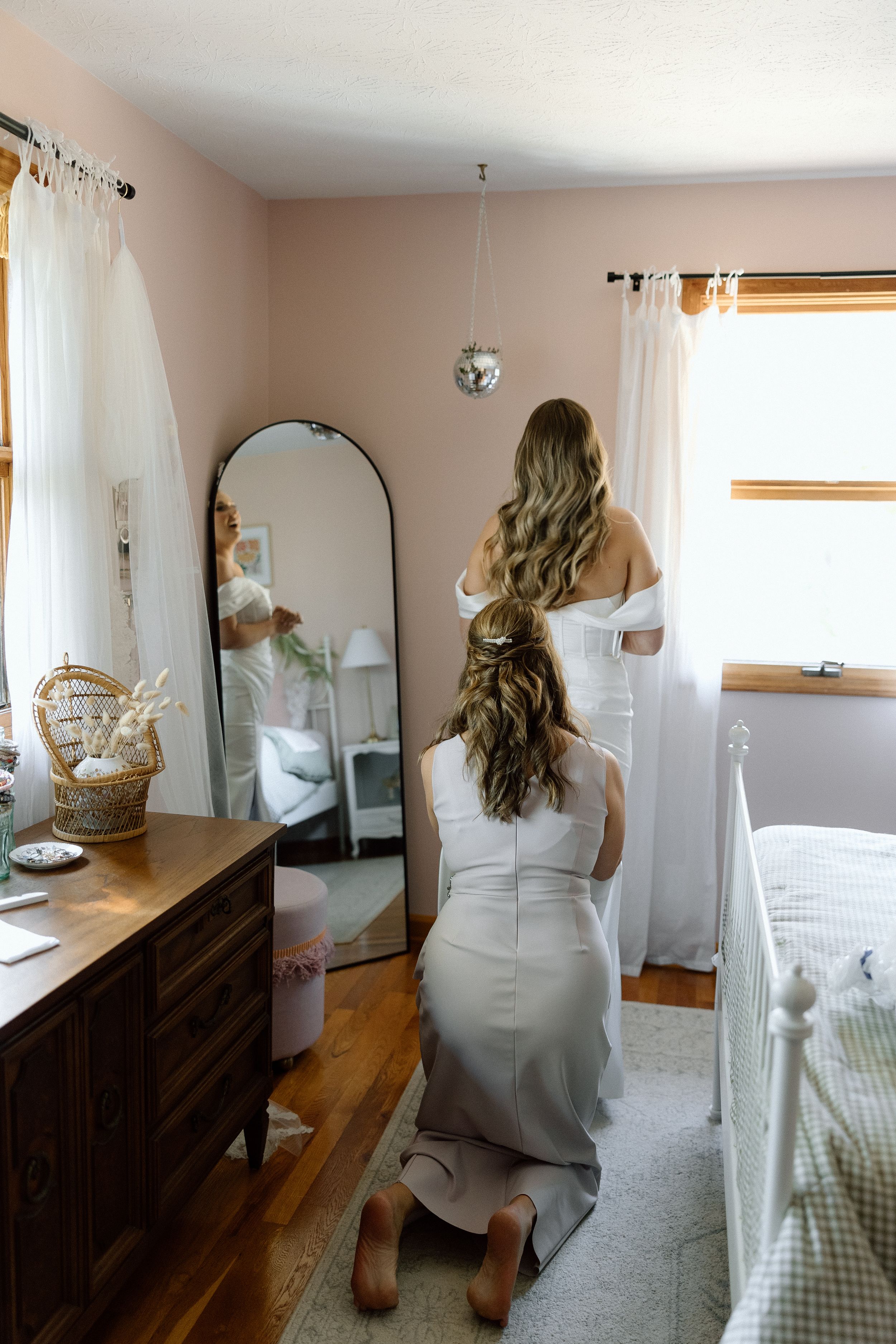 Person in a white dress looking at their reflection in a full-length mirror during wedding preparations.
