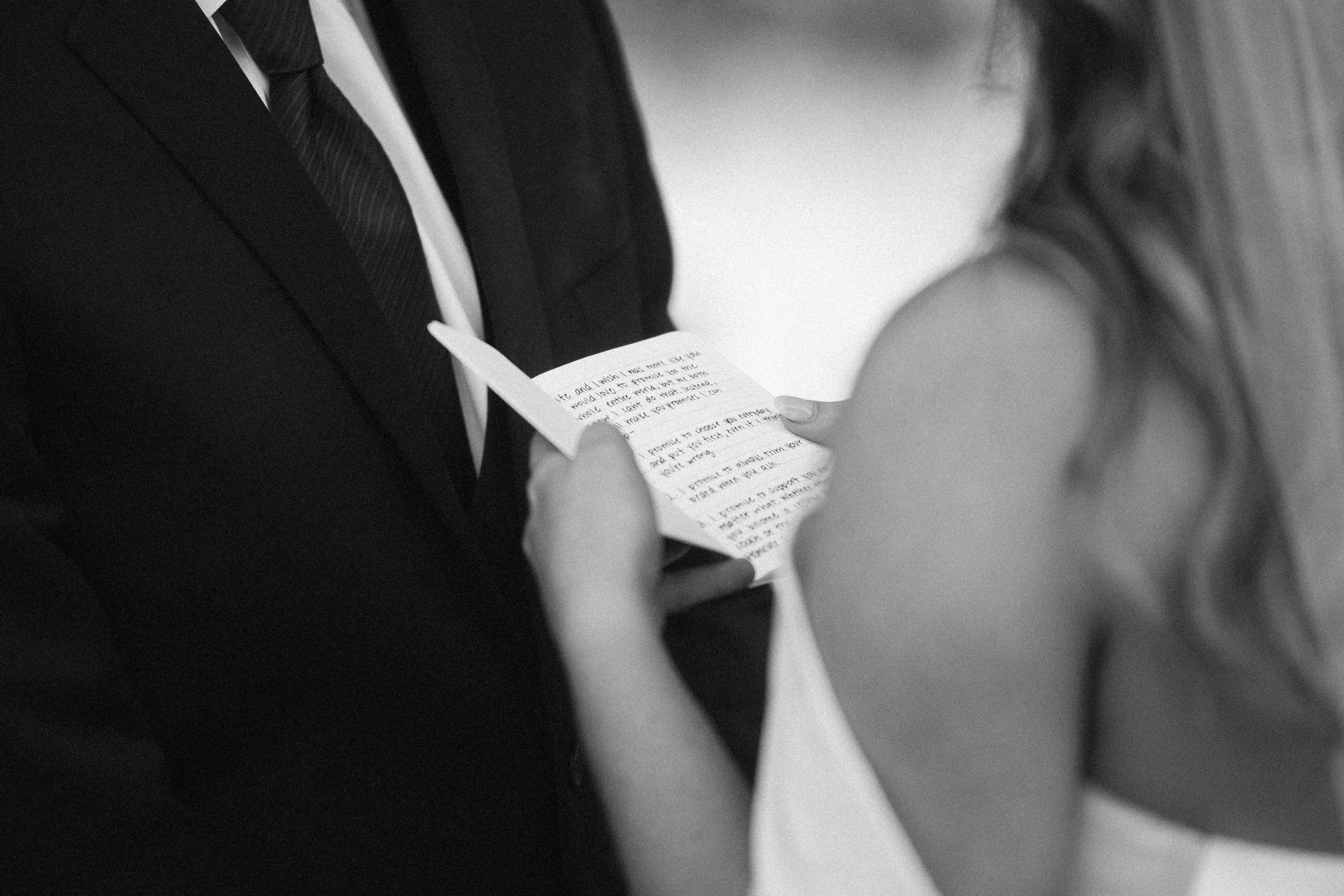 Black and white close-up of couple exchanging written vows during ceremony.