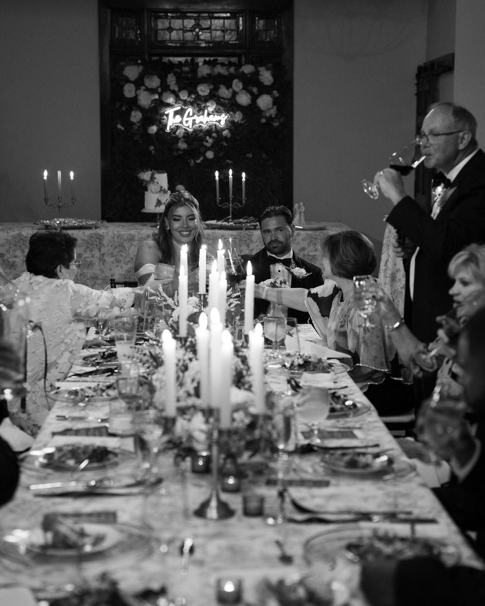 Black and white photo of an elegant dinner party with candelabras and guests gathered around a formal table setting.