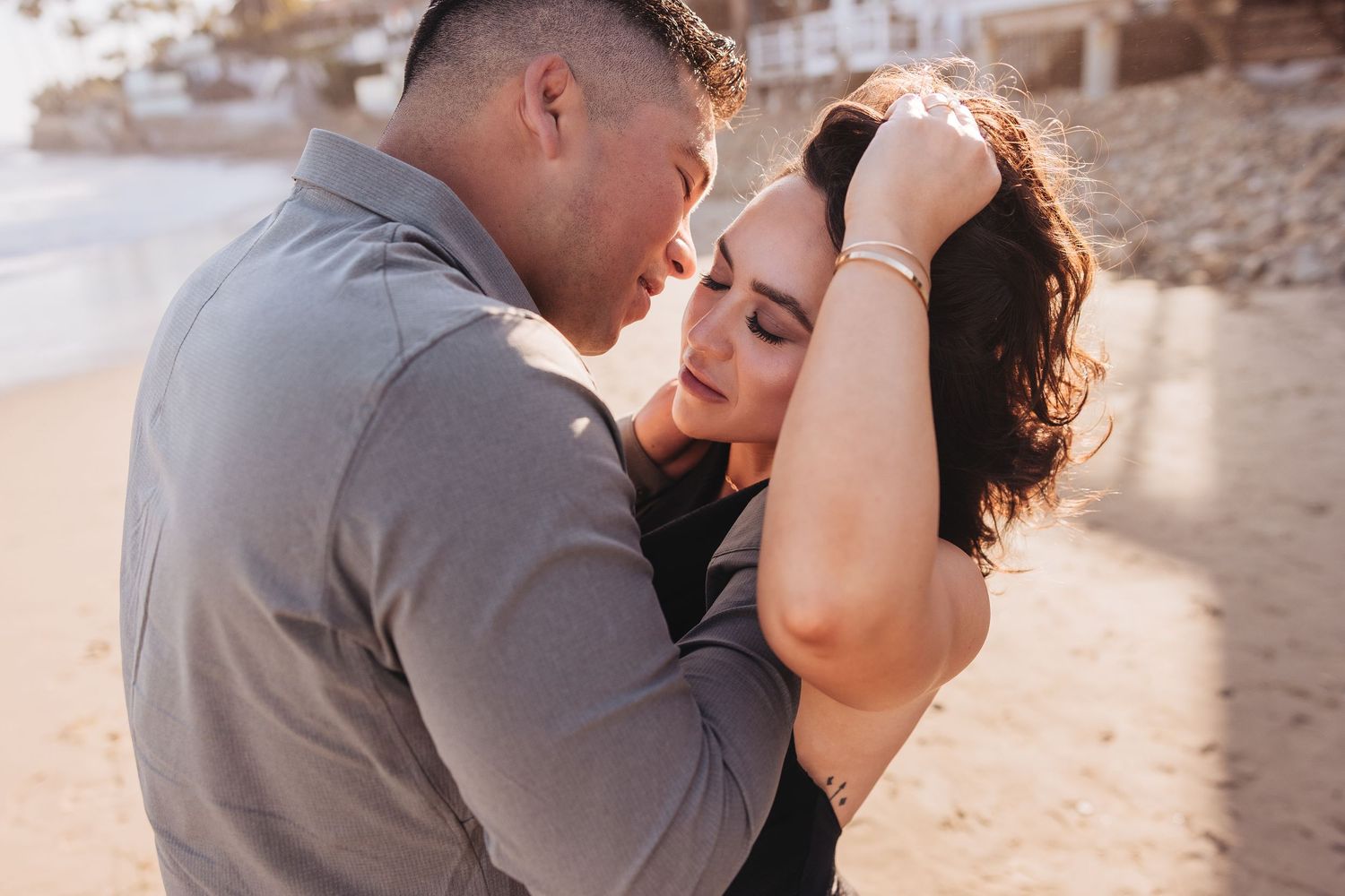 A loving couple embraces tenderly at sunset on a rocky beach while sharing an intimate moment.