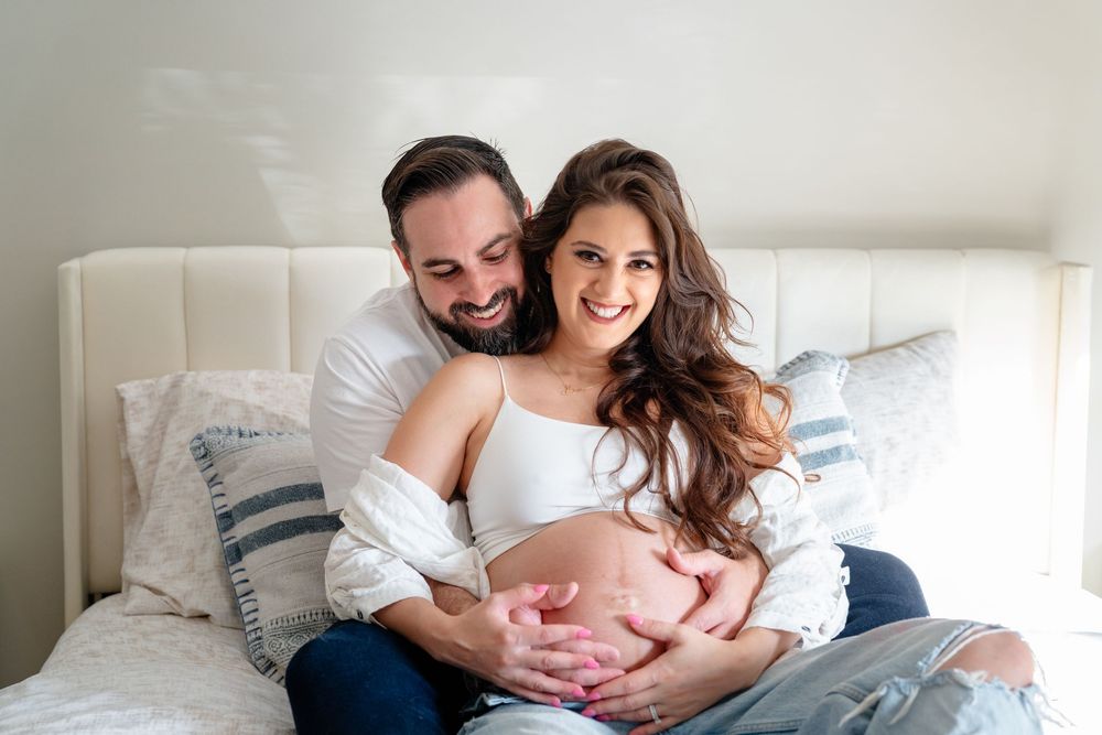 Intimate maternity photo session with couple relaxing together on white bedding.