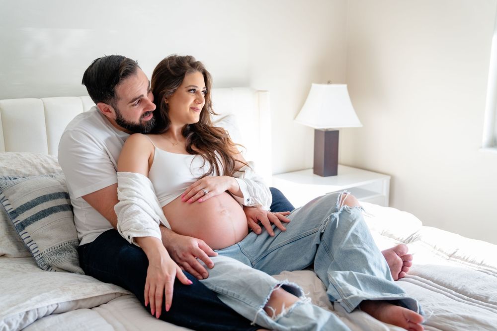 Expectant couple relaxing together on white bed in intimate moment.