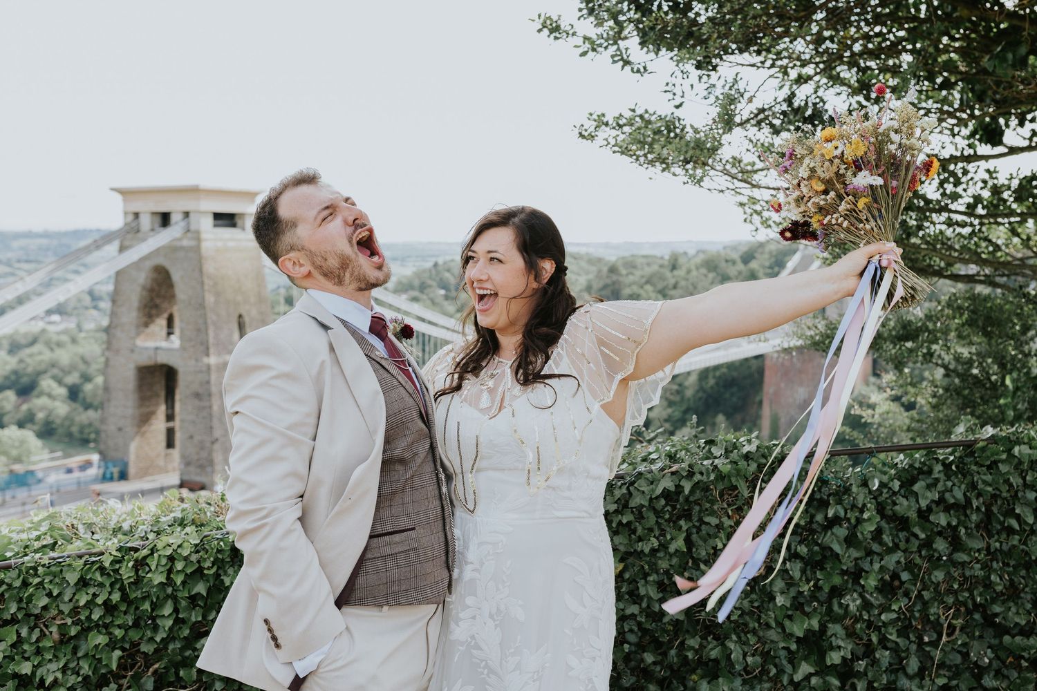 A cheerful wedding couple twirls and dances together outdoors with joy against a natural garden backdrop.