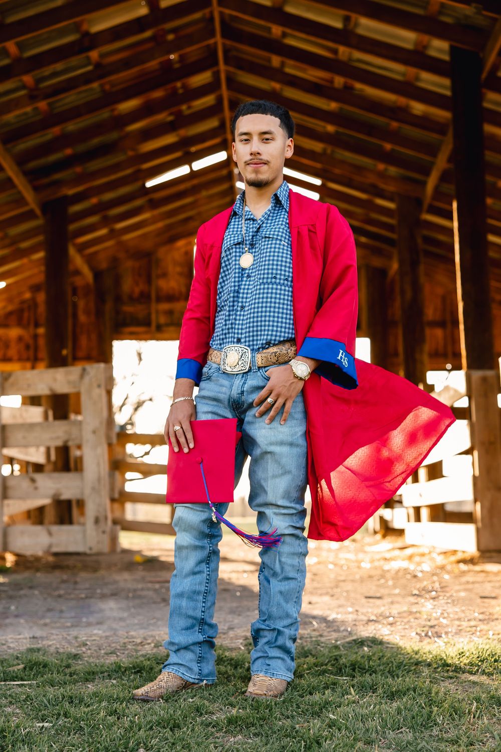 A person stands in a rustic barn wearing a bright red coat, gingham shirt, jeans and belt buckle in country western style.