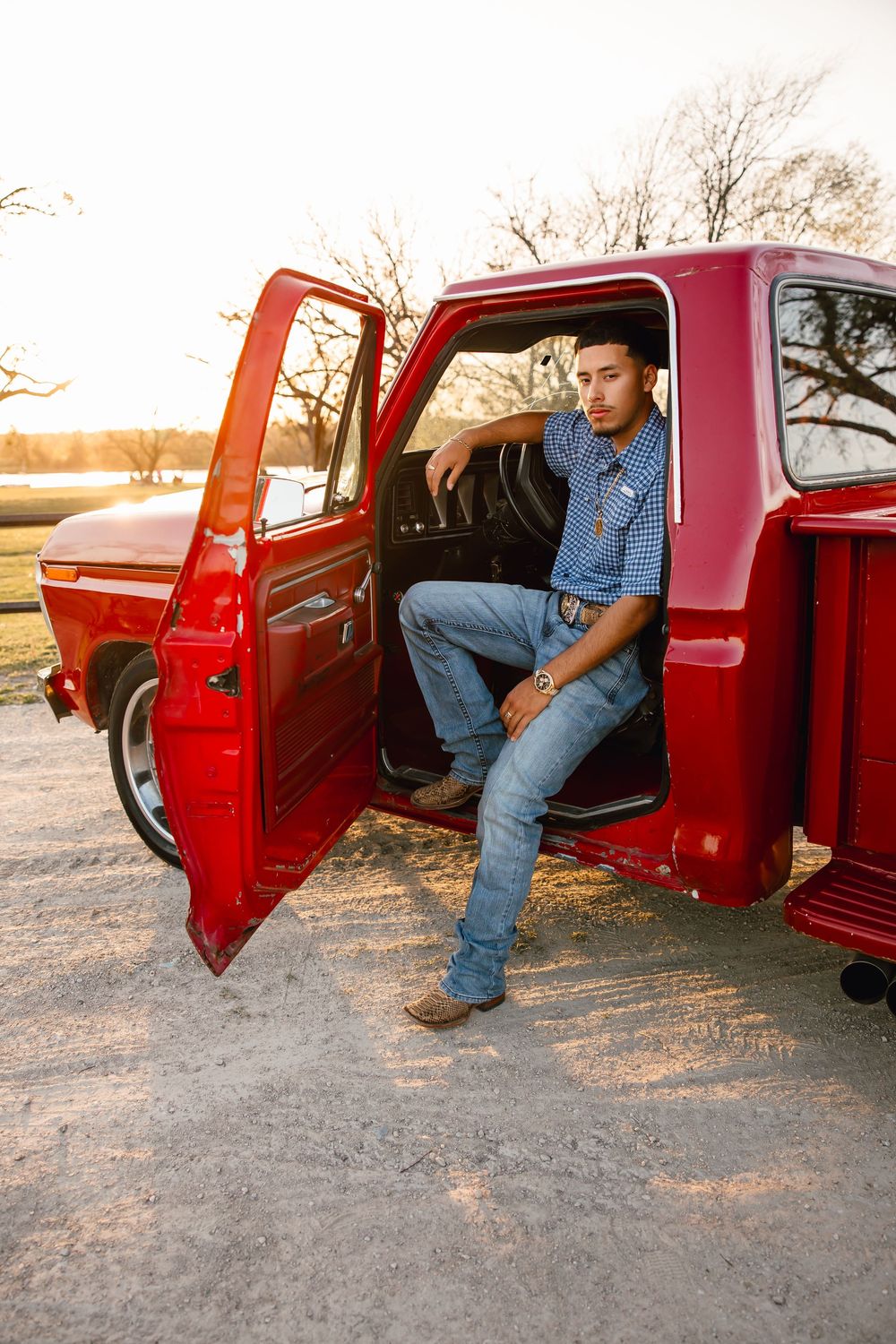 Person in denim sitting in a vintage red pickup truck with open door at sunset.