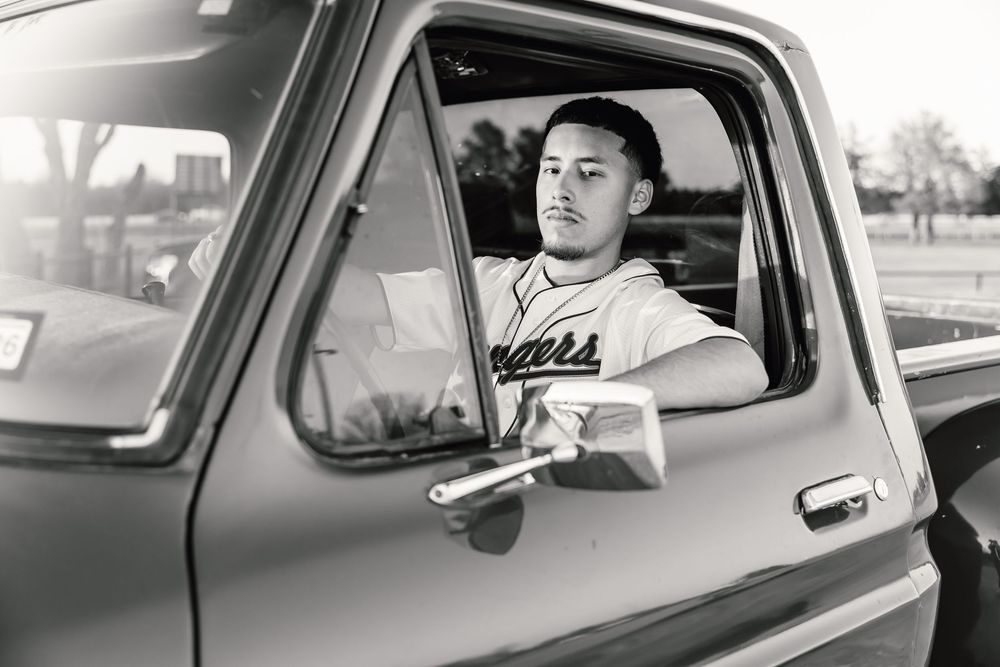 Black and white vintage photo showing a person sitting in the drivers seat of an old pickup truck wearing a sports team jersey.