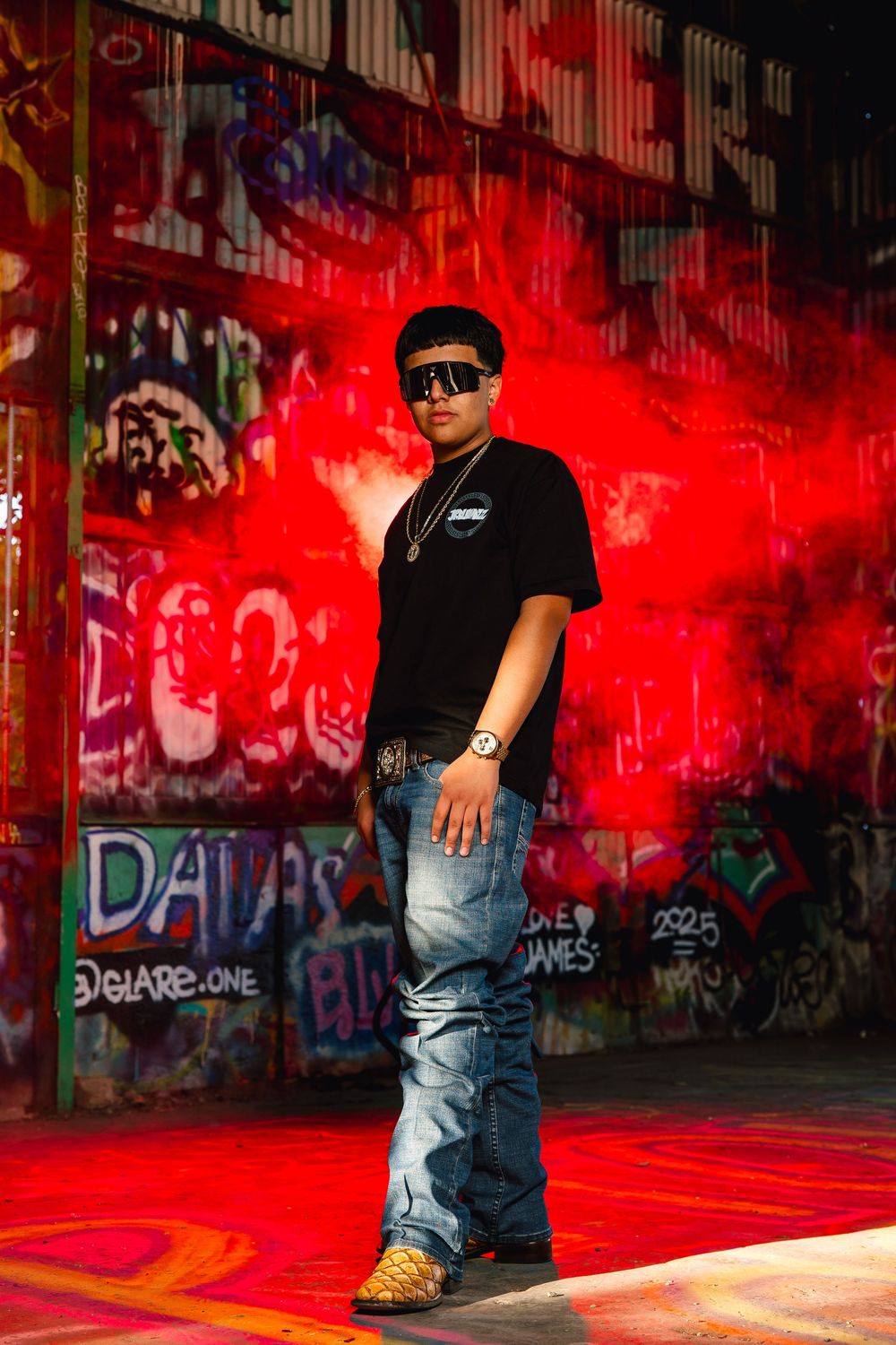 Urban portrait against vibrant red-lit graffiti wall with dramatic shadows and street art backdrop.