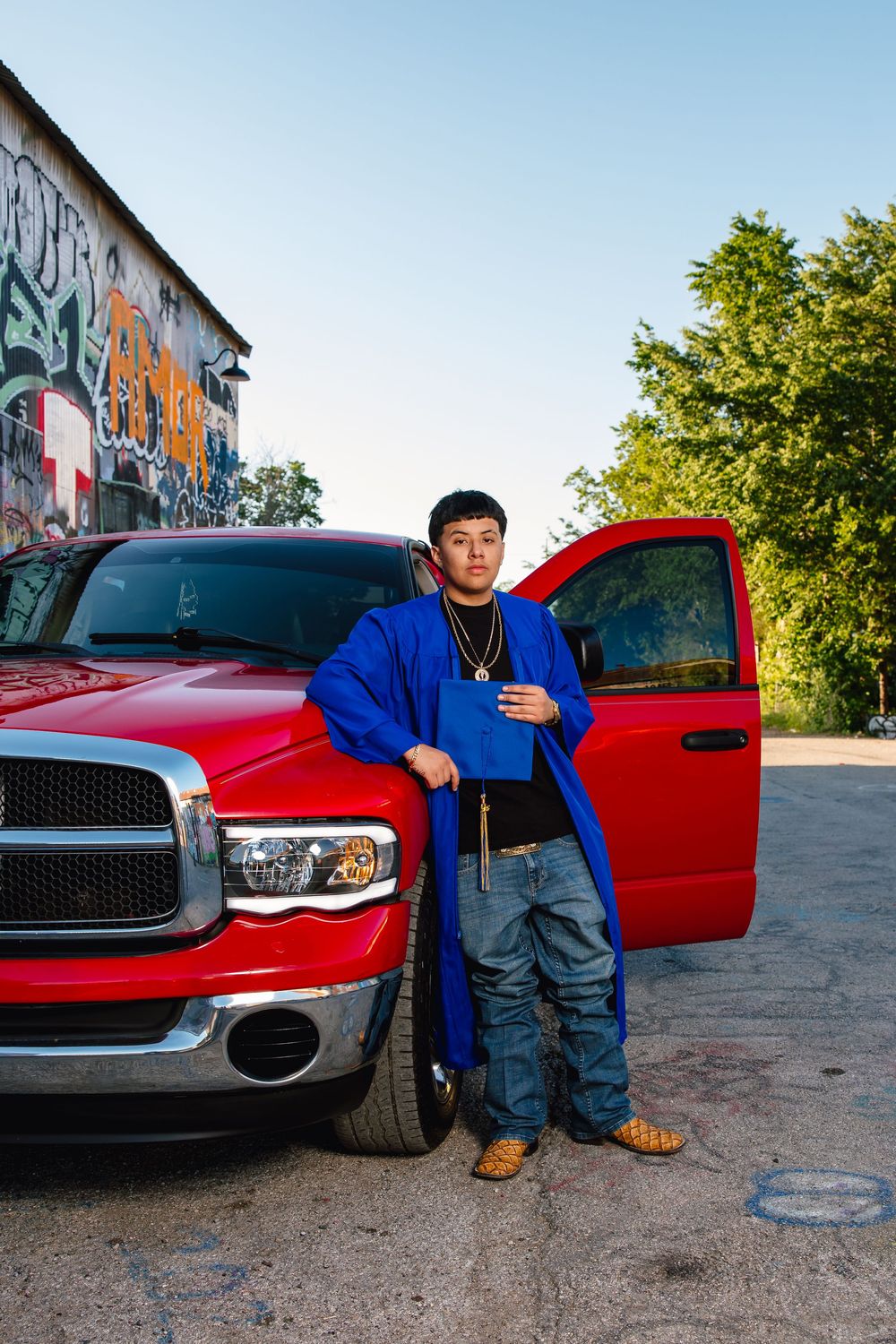 Person in a blue jacket stands next to a red Dodge Ram pickup truck with graffiti wall in background.