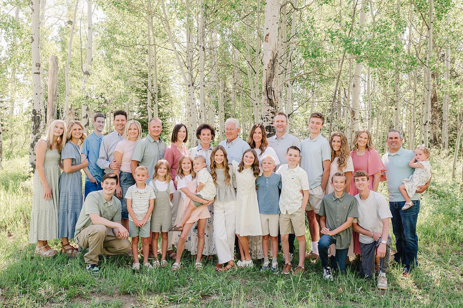 Large group wearing coordinated blue and white outfits poses together in a sunlit aspen forest setting.