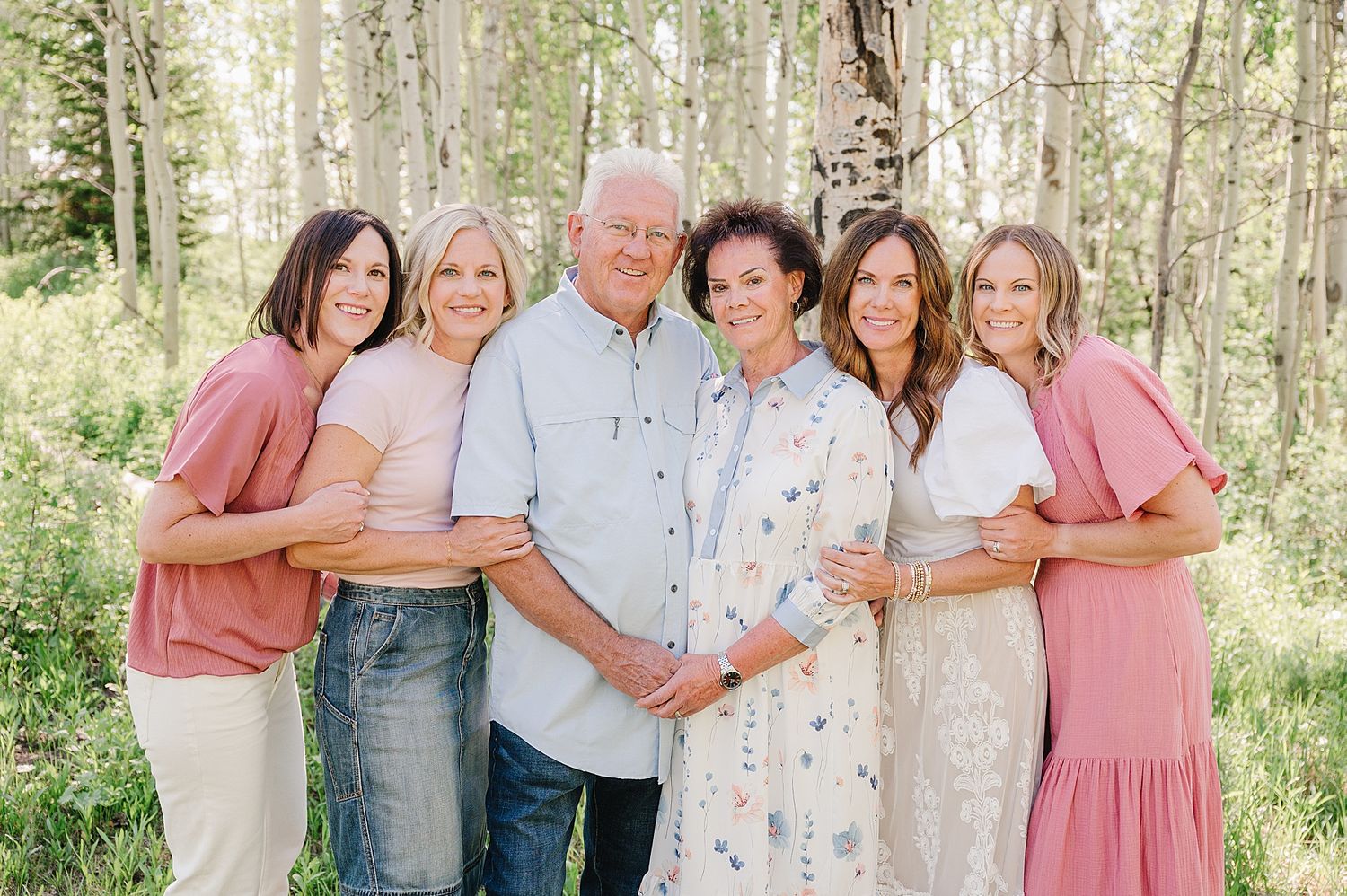 Group poses together in casual attire amongst white birch trees in a sunny woodland setting.