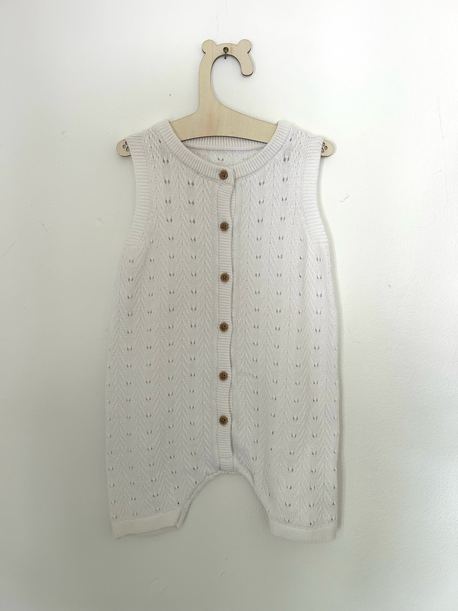 White baby romper with delicate pink embroidered floral design and ruffle details on straps.