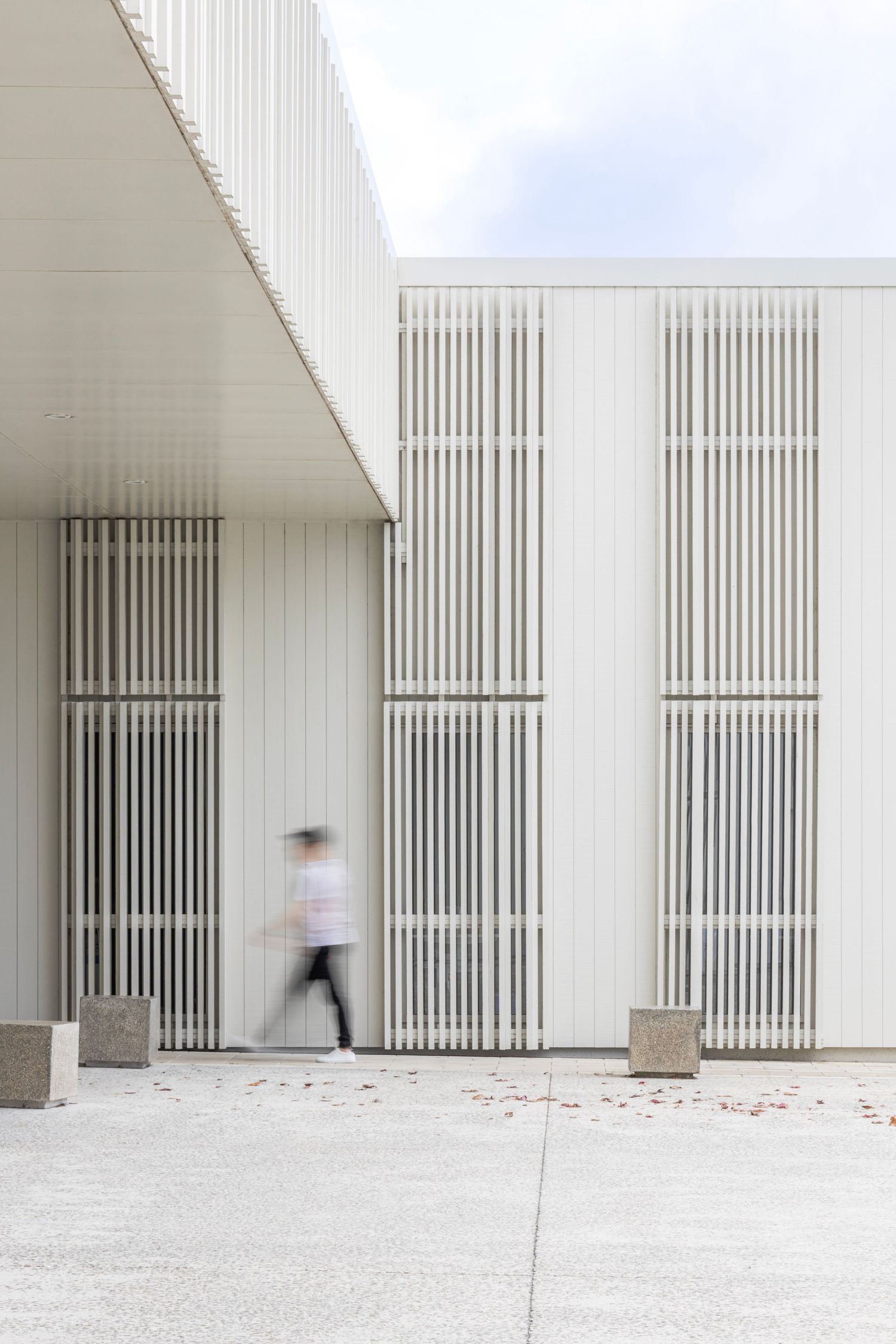 White building with vertical slats and a blurred figure walking past.