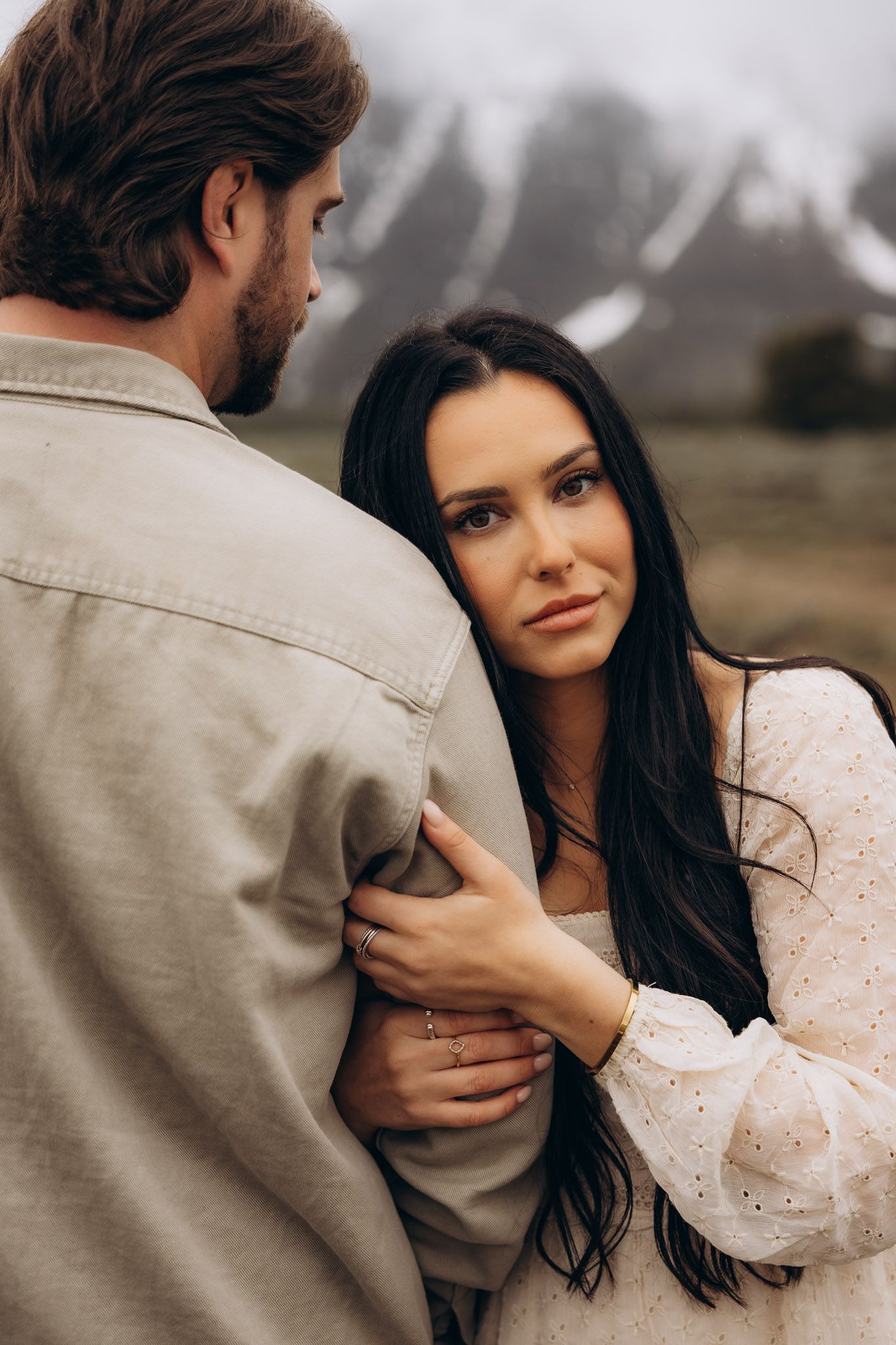 An intimate portrait of a couple sharing a tender moment outdoors, with snow-capped mountains visible in the background.