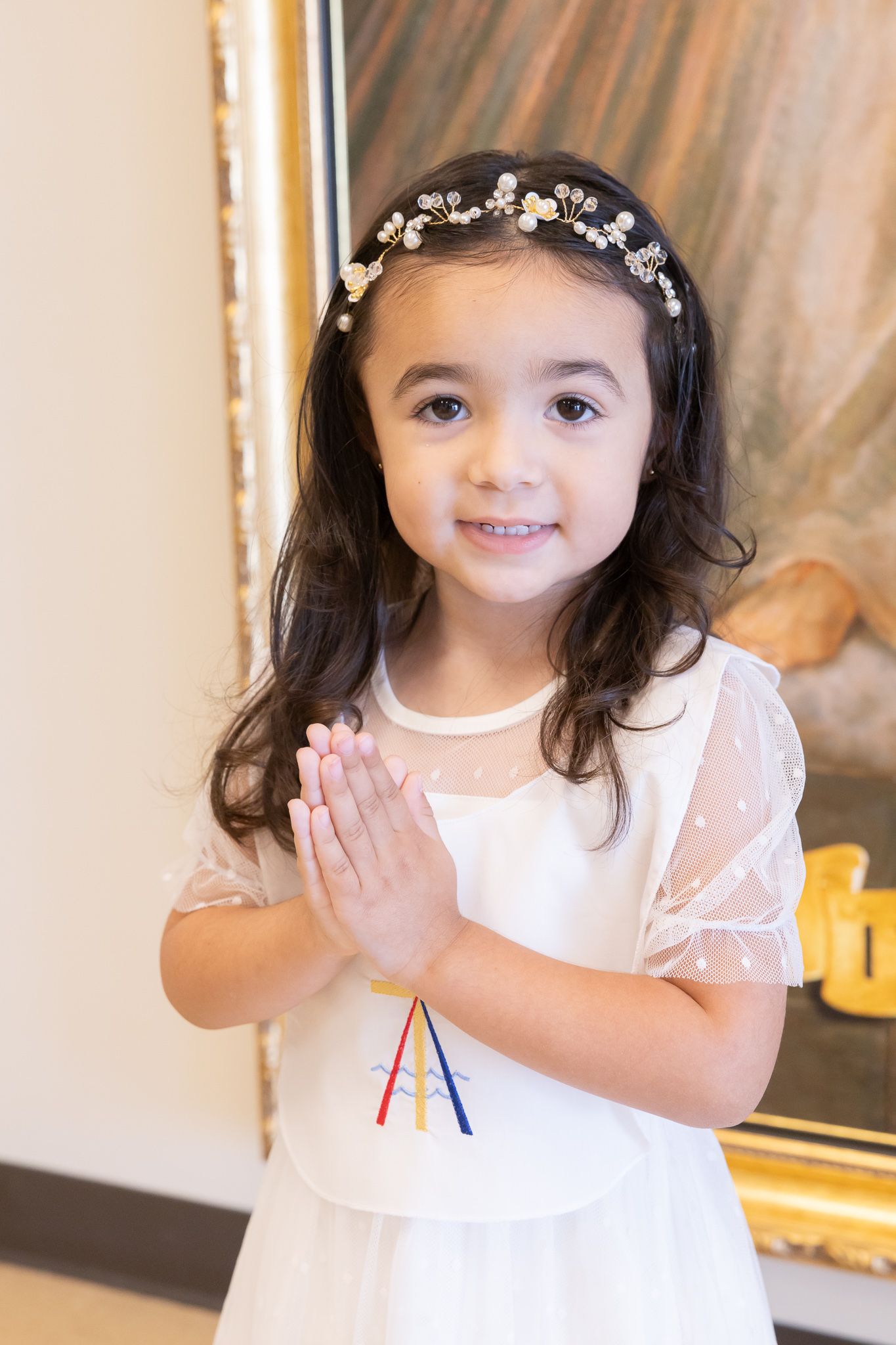 Young girl in white dress wearing floral headpiece and praying.