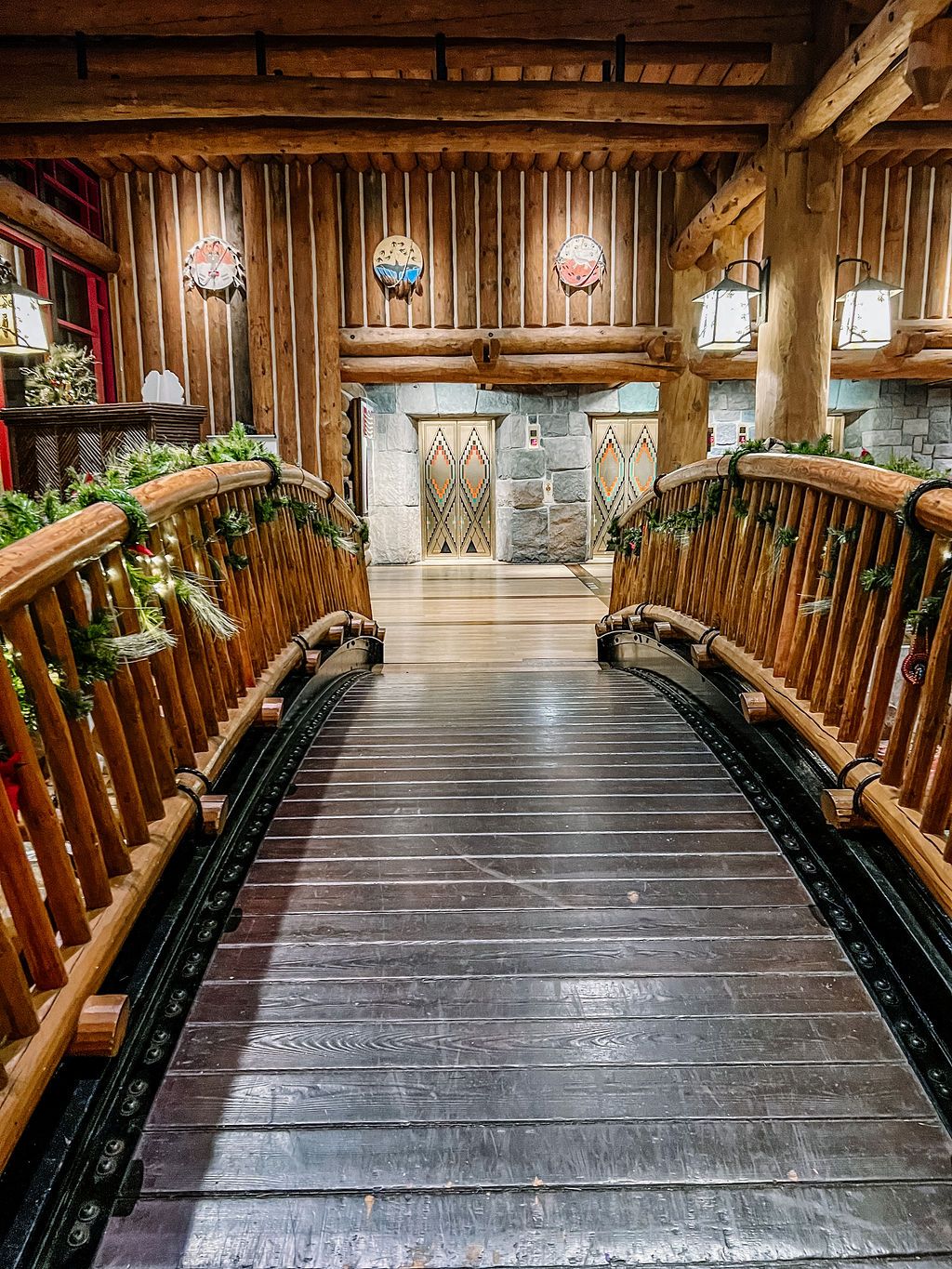 Wooden bridge walkway with rustic log railings and lantern lighting fixtures.