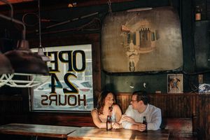 Couple enjoying drinks together at a dimly lit bar with vintage decor and neon signage.