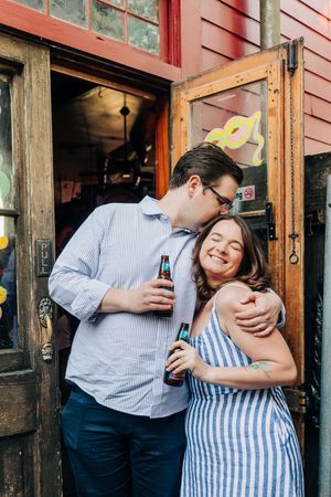 A couple shares an intimate moment together while holding drinks outside a red building.