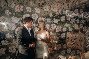 Couple sharing an intimate moment against a wall decorated with a romantic floral wallpaper pattern.