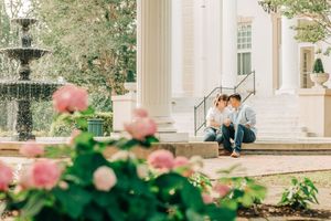 A white classical mansion with elegant columns and pink roses blooming in the foreground on a sunny day.