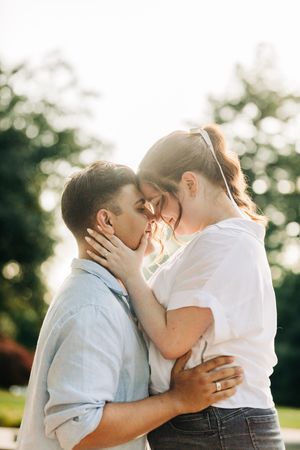 A romantic couple embraces outdoors in warm sunlight, sharing an intimate moment with their foreheads touching.