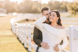 A romantic couple embraces by a white fence during golden hour, with gentle sunlight illuminating their special moment.