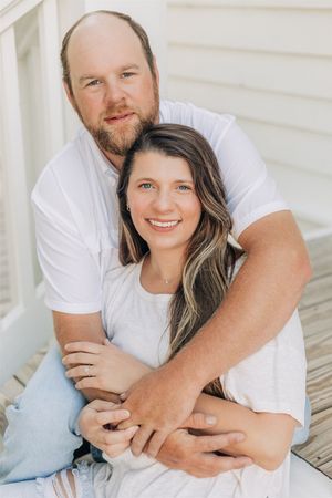 Couple in matching white t-shirts share an intimate embrace while sitting together outdoors.