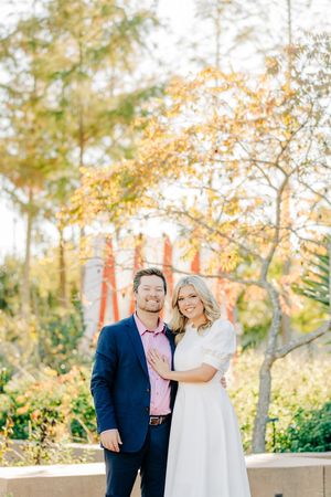 Couple poses together outdoors during autumn engagement session with golden sunlit trees in background.
