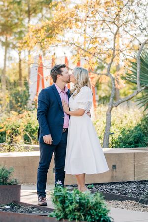 A couple shares a romantic moment in a garden setting with fall foliage and natural light during a photoshoot.