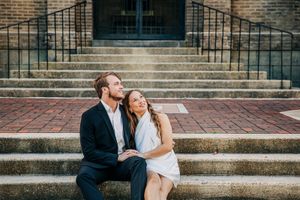 Two people share a joyful moment while sitting on brick steps outside a building with a romantic sunset glow.