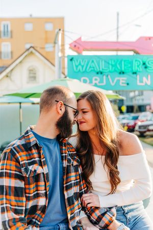 A couple sharing an intimate moment outside a retro-style drive-in restaurant with neon signage.