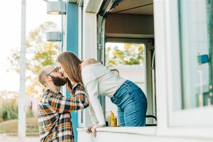 Young couple shares a playful moment at a drive-through window in casual outfits on a sunny day.