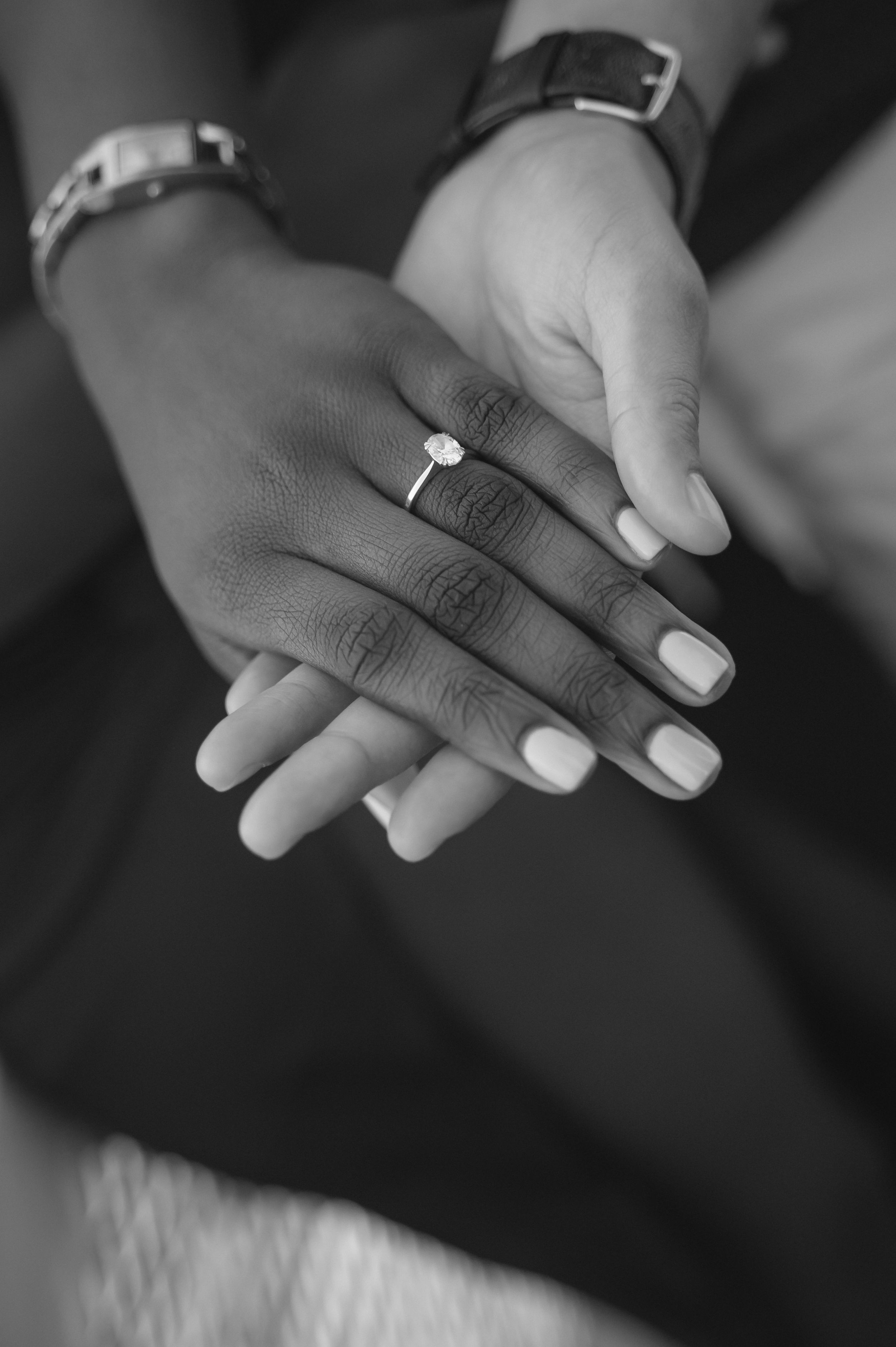 Black and white close-up of hands showing engagement ring with white manicured nails.
