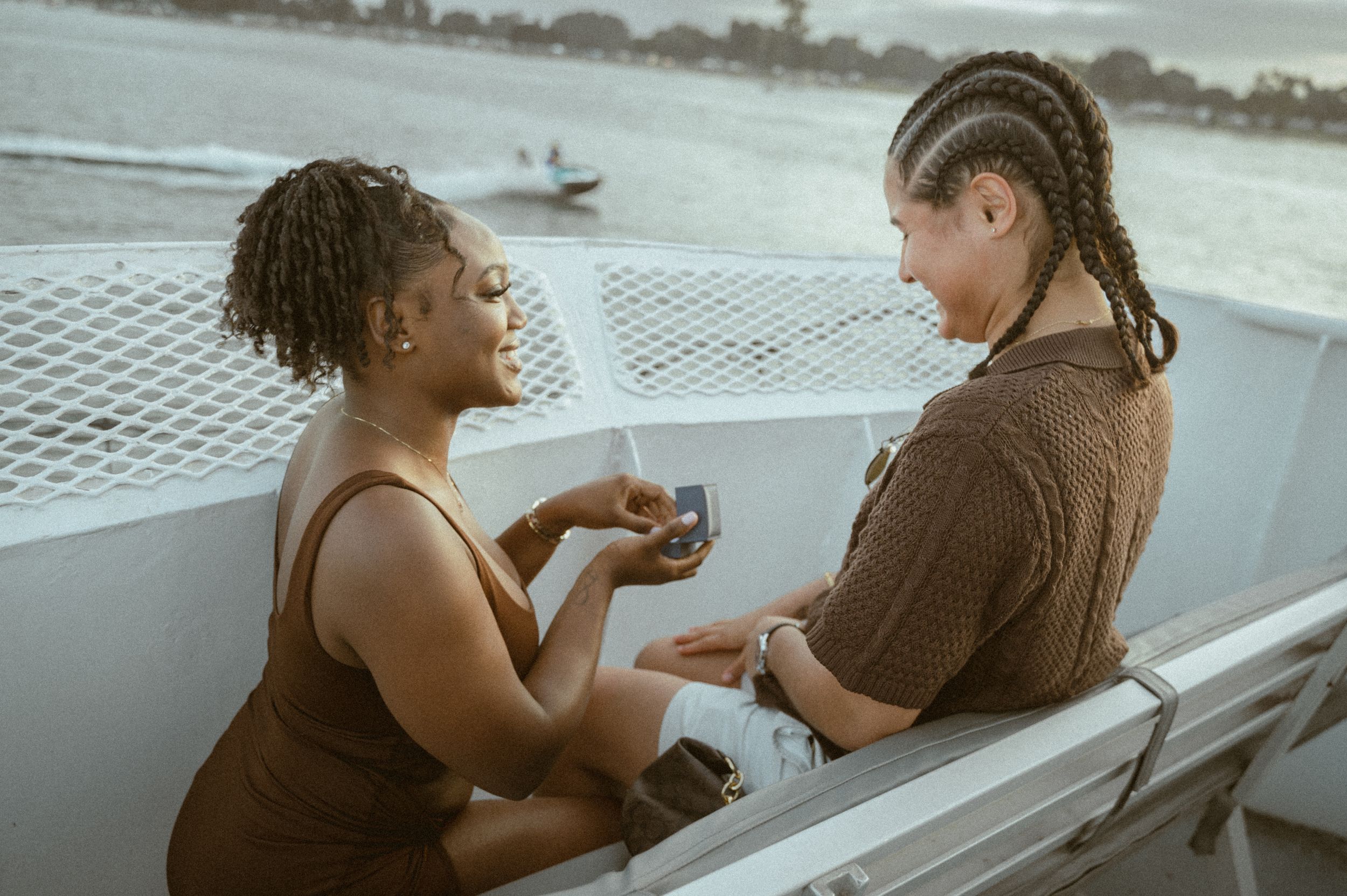A romantic proposal moment on a boat deck with water and coastline in the background.