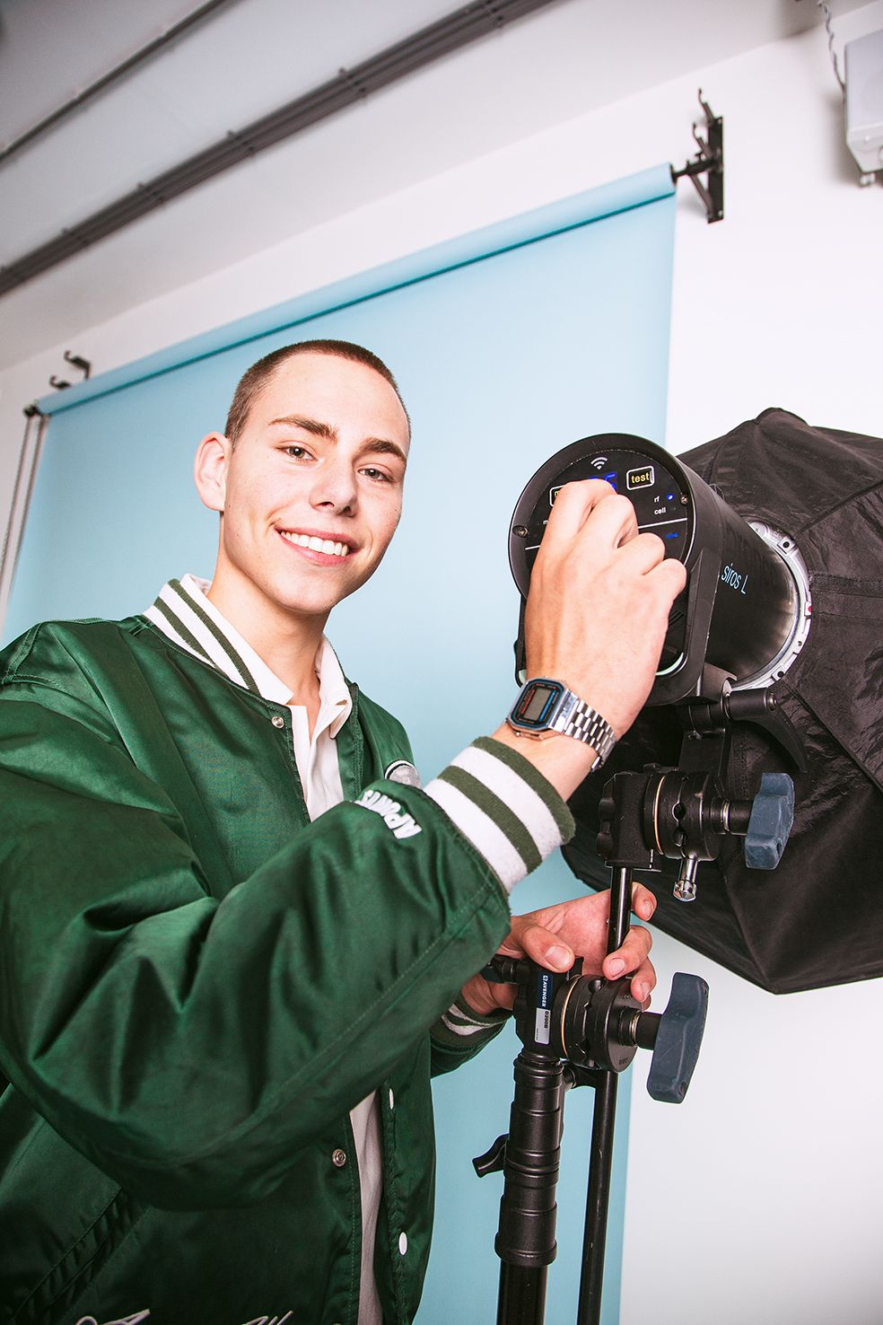 Person in green varsity jacket adjusts professional lighting equipment in studio setting.