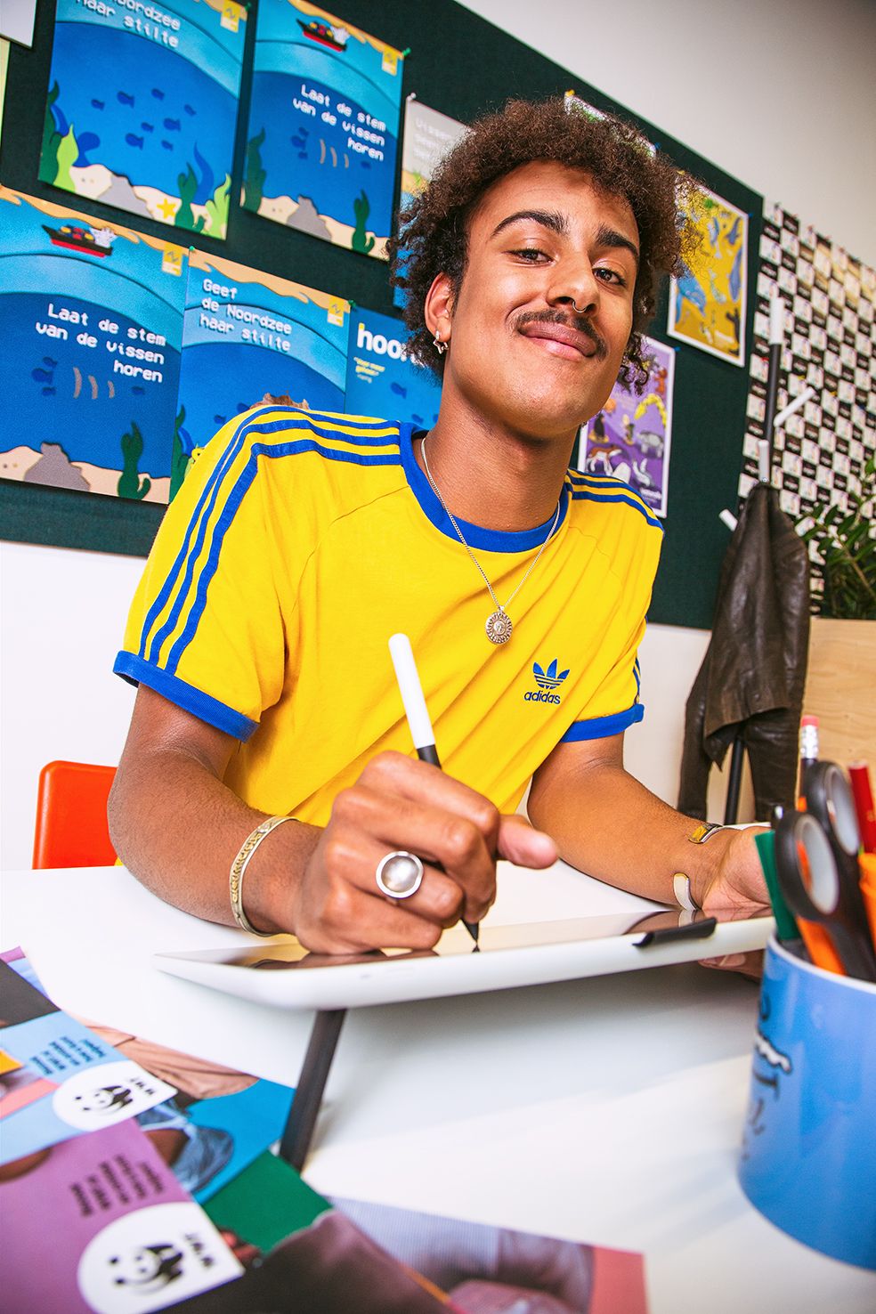 Student writing at desk with colorful educational posters displayed on wall behind.