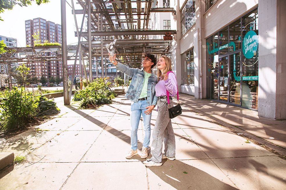 People walking through covered outdoor walkway with modern architecture and sunlit shadows.