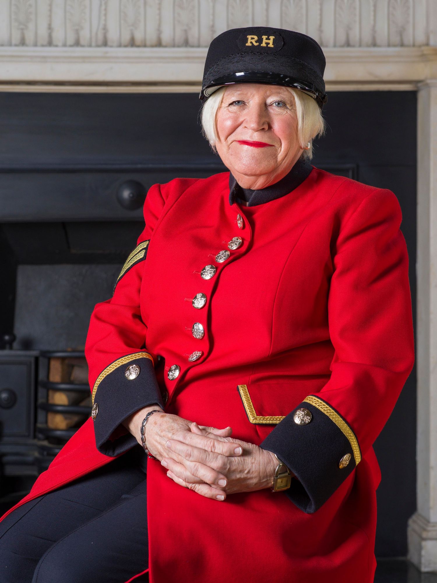Someone wearing a traditional red military-style uniform with gold buttons and black cap poses for a portrait.