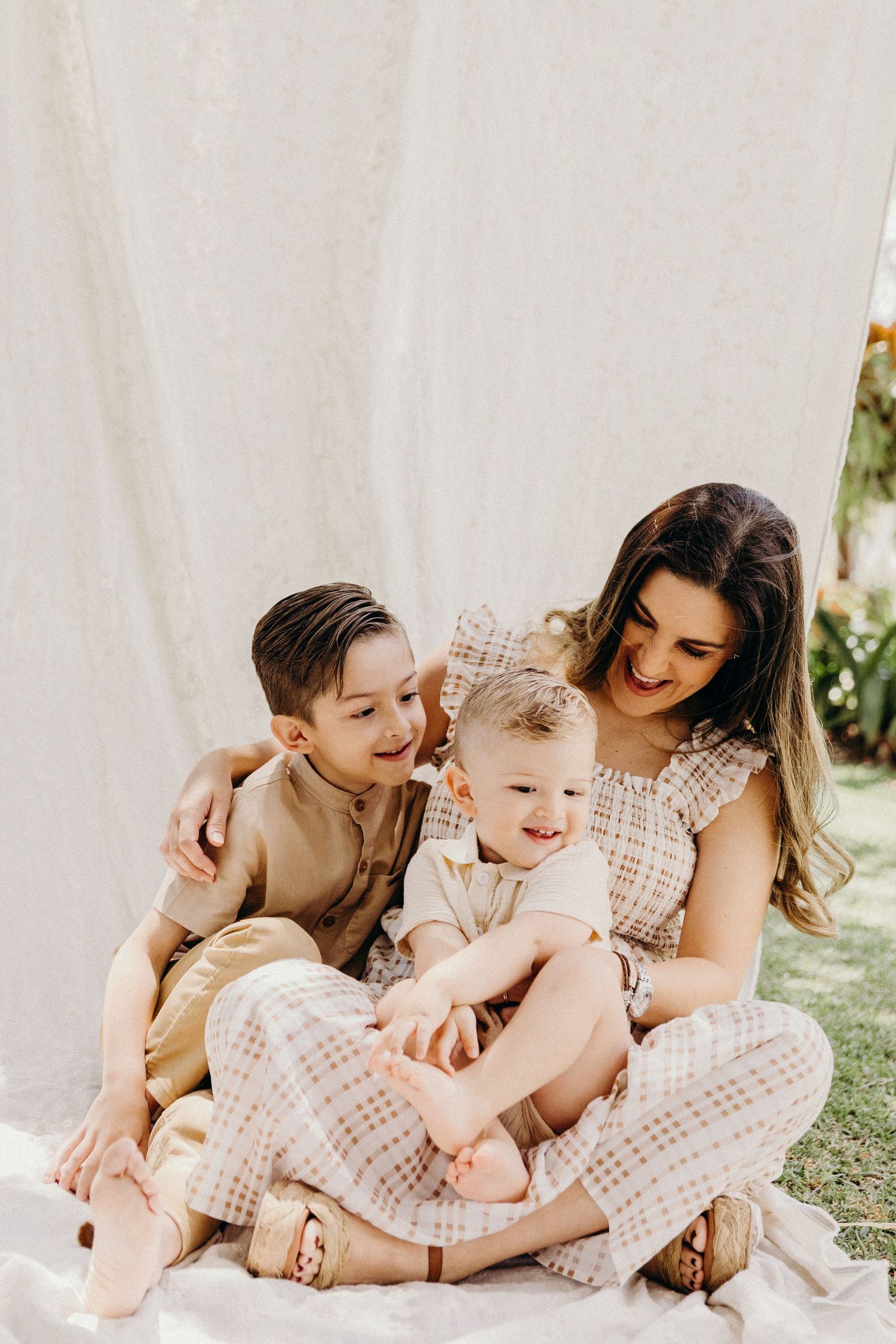 A couple poses with their small white puppy under a large tree trunk.