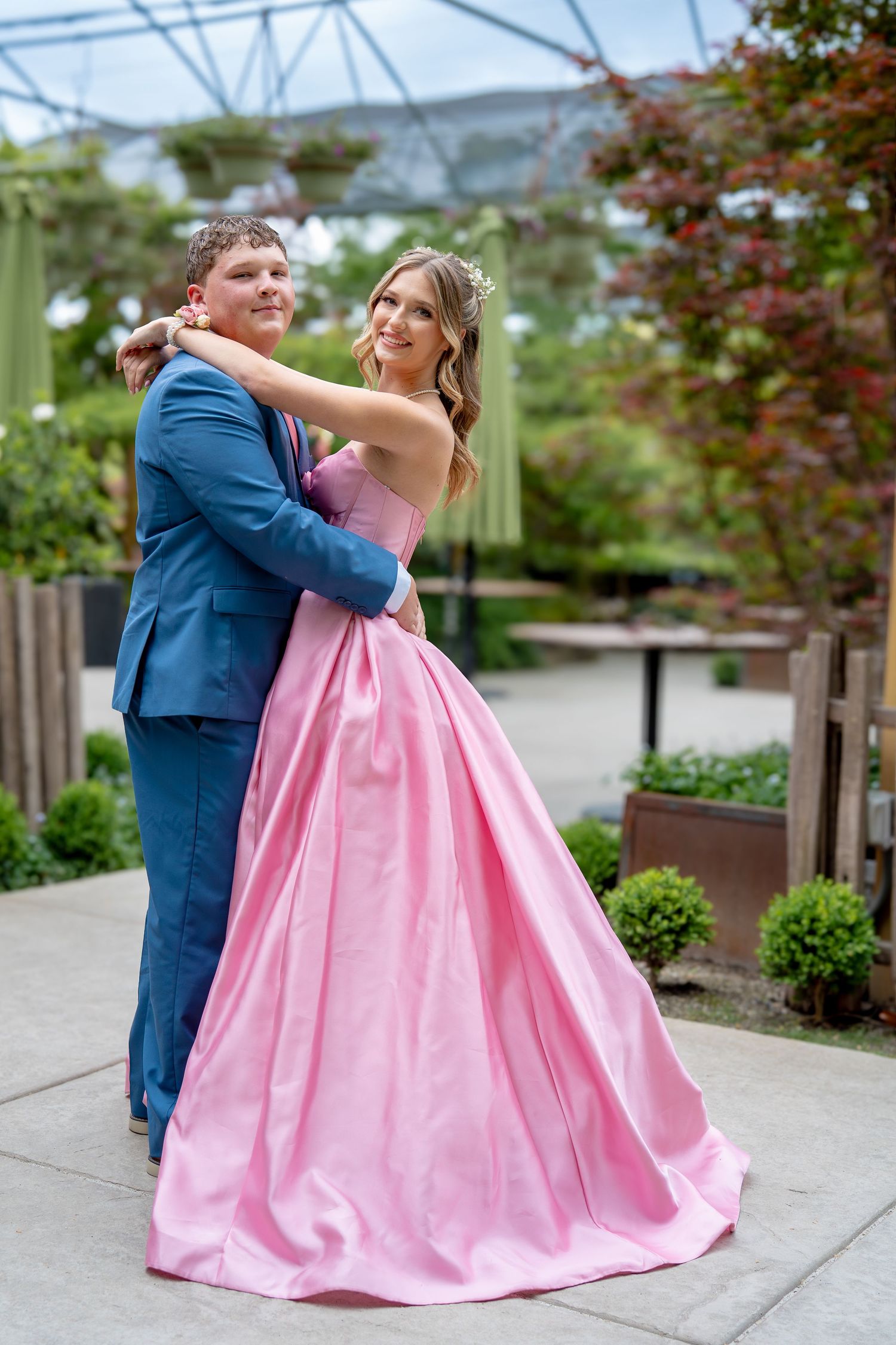 Couple dressed in purple bridesmaid dress and black suit posing playfully on concrete steps outdoors.