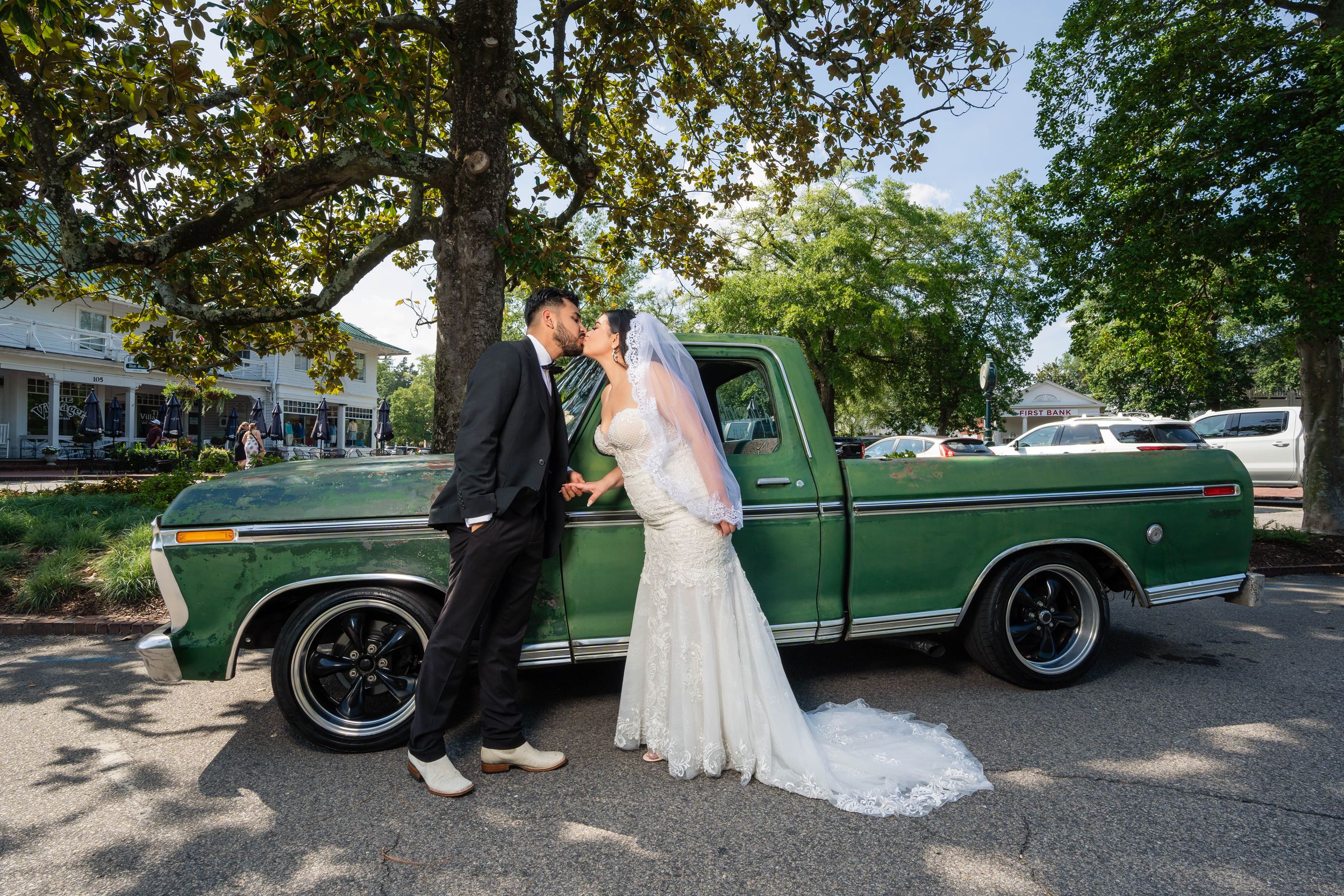 Classic wedding portrait with vintage green pickup truck under tree-lined street.