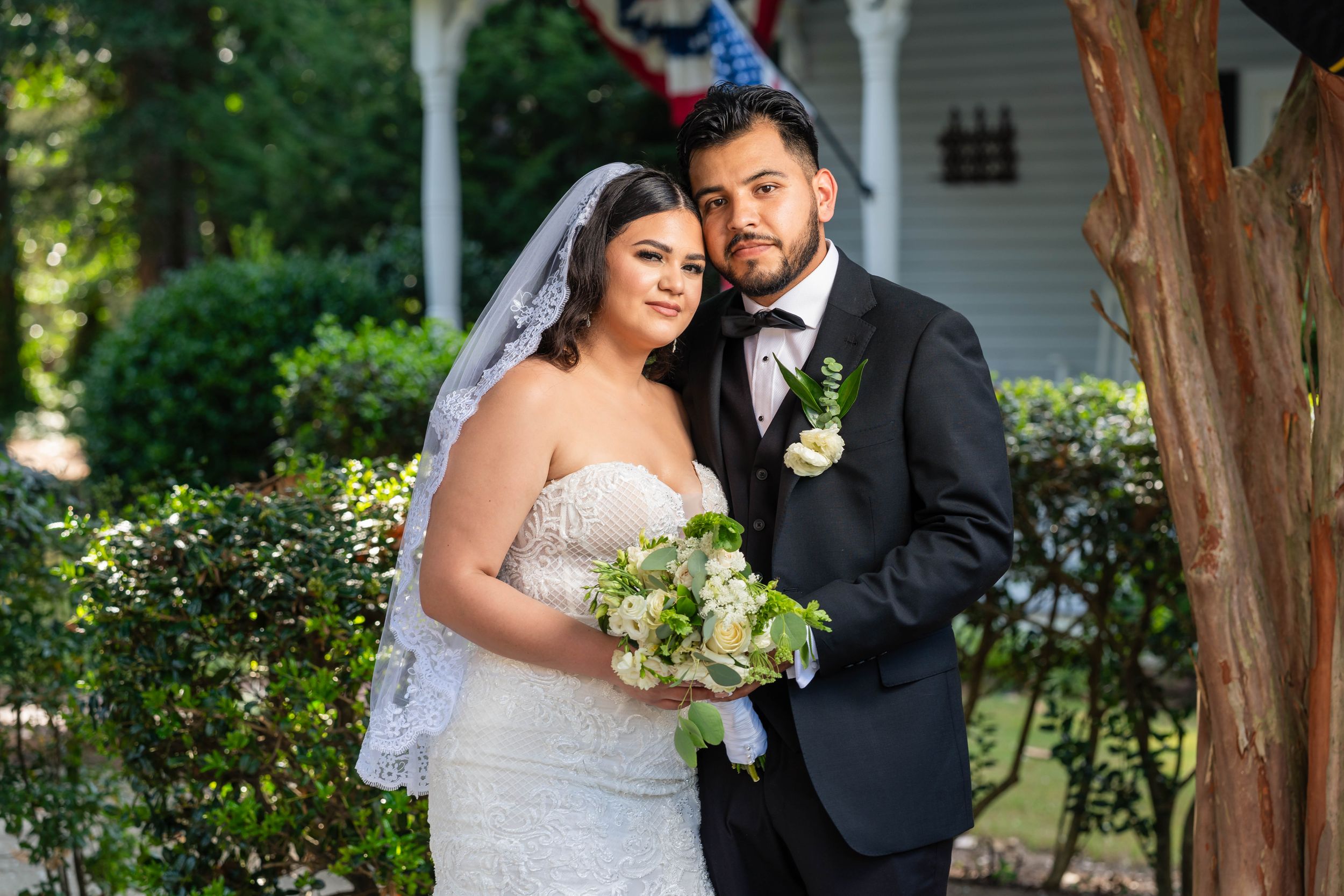 Joyful wedding portrait captured in front of lush garden greenery.