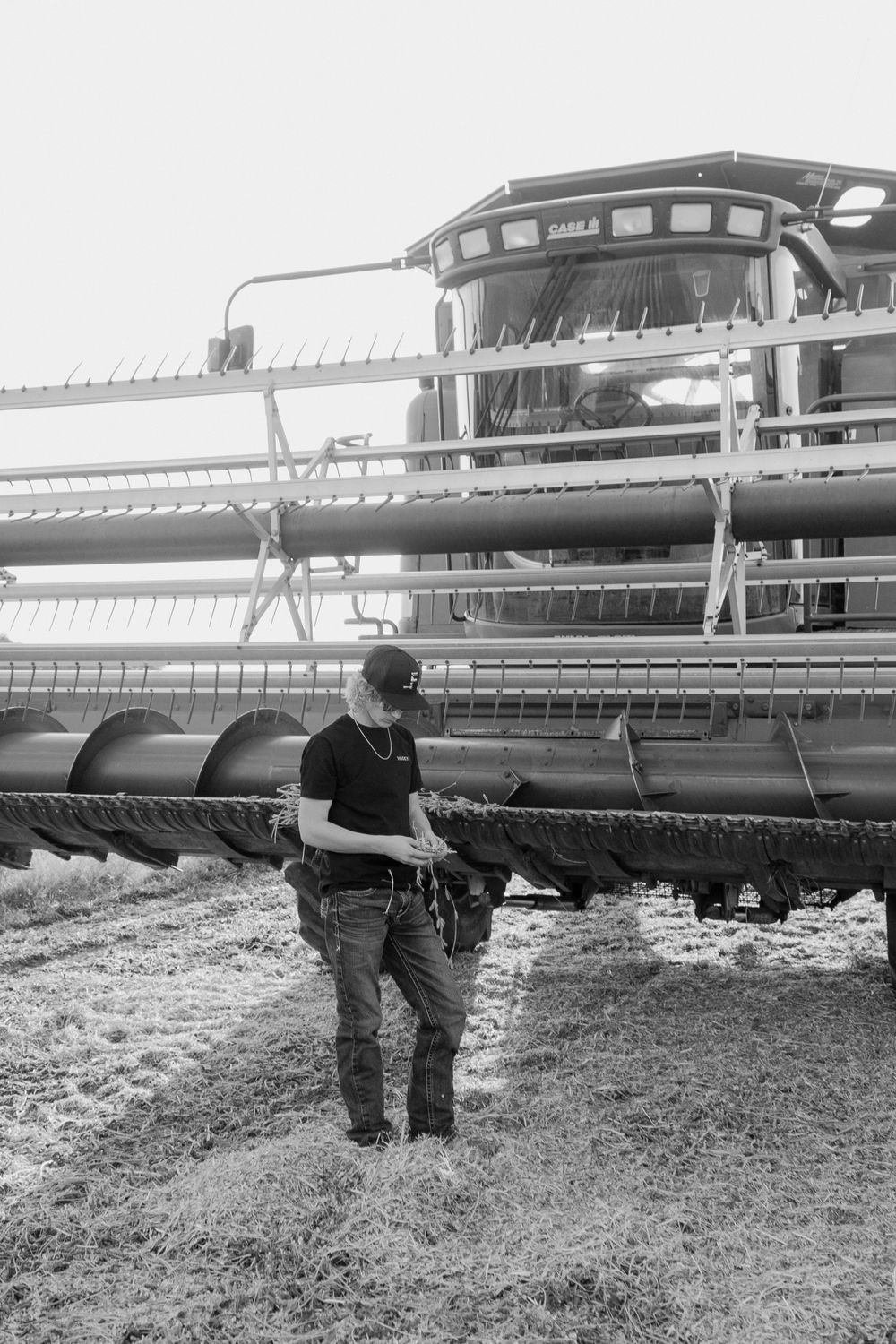 Black and white portrait of person standing by farm equipment outdoors.