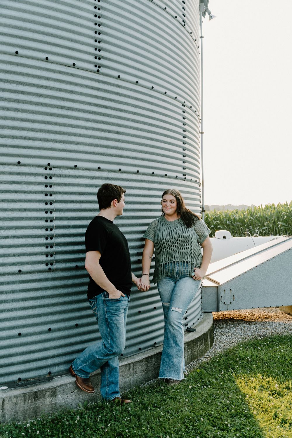 Couple standing beside a large metal grain silo on a farm.